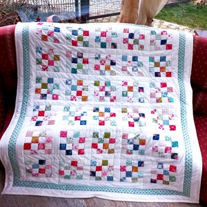 Könnte beinhalten: Eine weiße Steppdecke mit einem blauen und weißen Tupfenrand. Die Steppdecke besteht aus 36 Quadraten, jedes mit einem anderen Patchwork-Design mit verschiedenen Farben und Mustern.