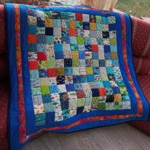 Könnte beinhalten: Eine blaue Patchwork-Decke mit rotem und orangefarbenem Rand. Die Decke besteht aus vielen verschiedenen Stoffquadraten, jedes mit einem anderen Muster. Die Decke ist perfekt für ein Baby oder Kleinkind.