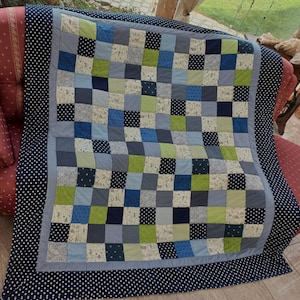 Könnte beinhalten: Eine Patchwork-Decke mit einem dunkelblauen Rand und weißen Punkten. Die Decke besteht aus Quadraten in Blautönen, Grün- und Weißtönen.