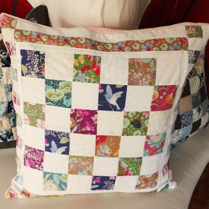 Può includere: Un cuscino bianco con un design a patchwork che presenta una varietà di motivi floreali e di uccelli. Il cuscino è composto da quadrati di tessuti diversi, ognuno con un design unico. Il cuscino è un'ottima aggiunta a qualsiasi arredamento per la casa.