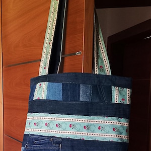 Può includere: Una borsa tote in denim blu con un bordo in tessuto a fantasia floreale. La borsa è realizzata in denim riciclato e presenta un design patchwork.