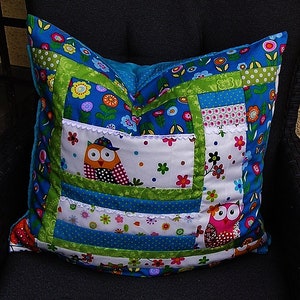 Könnte beinhalten: Ein blaues und grünes Patchwork-Kissen mit zwei Eulenmotiven. Die Eulen tragen Hüte und haben farbenfrohe Details. Das Kissen ist mit Blumen und Punkten verziert.