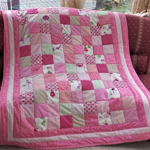 May include: A pink and green patchwork quilt with a variety of patterns and designs. The quilt is made up of squares and is edged with a pink border.