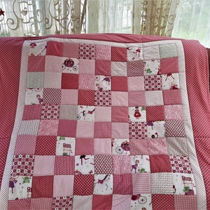 Könnte beinhalten: Eine rosafarbene und weiße Patchwork-Decke mit verschiedenen Mustern und Designs. Die Decke besteht aus Quadraten und zeigt Bilder von Feen, Kutschen und anderen fantasievollen Designs.