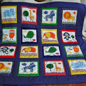 Könnte beinhalten: Eine blaue und weiße Babydecke mit verschiedenen Tier- und Naturmotiven. Die Decke besteht aus 16 Quadraten, jedes mit einem anderen Design. Zu den Tieren gehören ein Zebra, ein Löwe, ein Elefant, ein Affe, ein Vogel, ein Flusspferd und eine Eule. Die Naturmotive umfassen einen Baum, eine Sonne und eine Wolke.