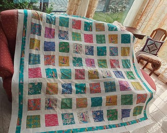 Può includere: Una trapunta patchwork caratterizzata da una griglia di quadrati di tessuto colorati nelle tonalità del verde acqua, rosa, giallo e verde, separati da strisce bianche. La trapunta presenta un bordo verde acqua e vari motivi floreali su ogni quadrato.