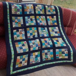Könnte beinhalten: Eine blaue und grüne Patchwork-Decke mit quadratischem Muster. Die Decke besteht aus vielen verschiedenen Stoffen und hat einen blauen Rand.