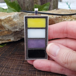 May include: A silver pendant necklace with a rectangular charm featuring four horizontal stripes in yellow, white, purple, and black. The charm is set in a silver frame.