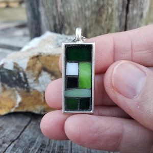 May include: A silver pendant with a rectangular mosaic design. The mosaic is made of small green, white, and black glass tiles.