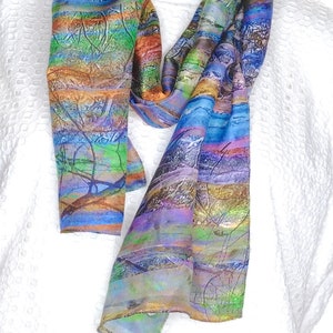 May include: A colourful silk scarf with a striped pattern and abstract art design. The scarf is made of soft, flowing silk and features a variety of colours, including blue, green, purple, orange, and yellow.