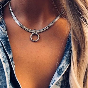 May include: A silver chain choker necklace with a large silver ring pendant.