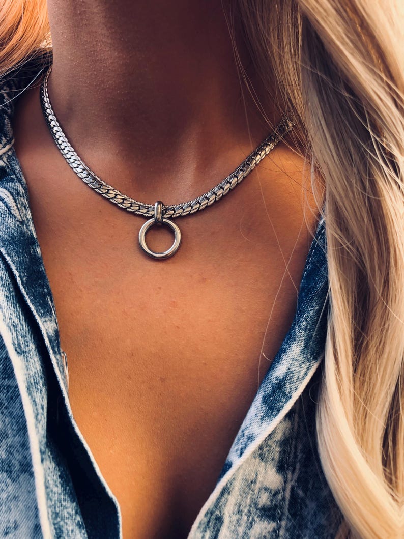 May include: A silver chain choker necklace with a large silver ring pendant.