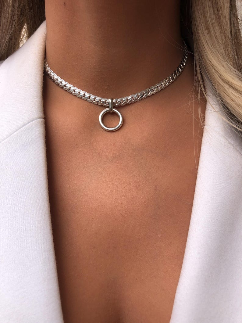 May include: A silver chain choker necklace with a large silver ring pendant.
