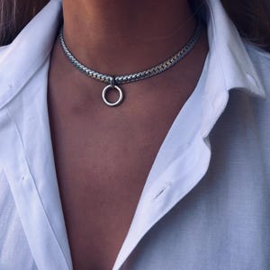 May include: A silver chain choker necklace with a large silver ring pendant.