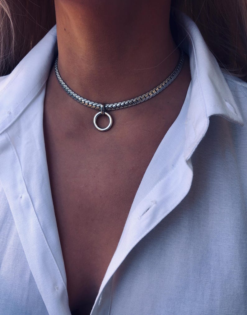 May include: A silver chain choker necklace with a large silver ring pendant.