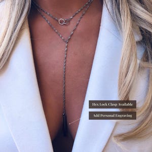 May include: A silver-toned double-layered necklace featuring a delicate twisted chain, two small interlocking rings at the collarbone, and a vertical bar pendant. Text on the image reads: Hex Lock Clasp Available and Add Personal Engraving.