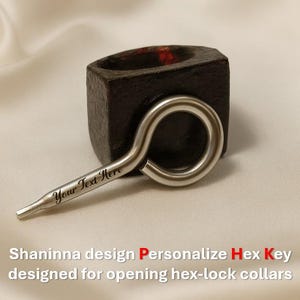 Puede incluir: Un objeto de madera oscura y cuadrada con una abertura circular, combinado con una llave hexagonal plateada. La llave tiene un bucle y un extremo puntiagudo con el texto "Your Text Here". También se ve el texto "Shaninna design Personalize Hex Key designed for opening hex-lock collars".