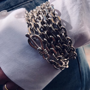 Puede incluir: Un brazalete de cadena de plata con múltiples eslabones y un cierre grande de plata.