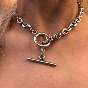 Può includere: Una collana a catena d'argento con una grande chiusura rotonda aperta e una chiusura a T.