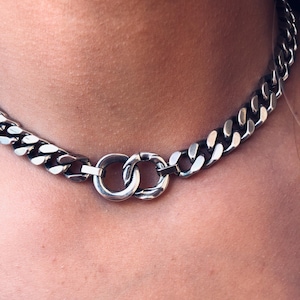 May include: A silver chain necklace with a double ring clasp. The chain is a curb style with a flat, rectangular link.