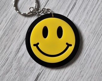 May include: A black and yellow smiley face keychain with a silver key ring.