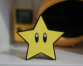 May include: A yellow star-shaped decoration with black outlines and two oval eyes. The star is a popular video game character. Other yellow items are visible in the background, including a Pac-Man-shaped object and a handheld gaming device.