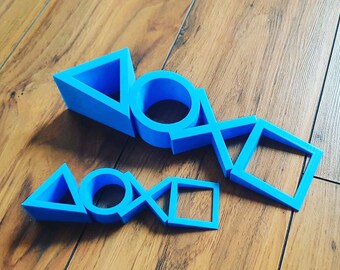 May include: Two sets of blue plastic PlayStation controller symbols. The larger set includes a triangle, circle, X, and square. The smaller set includes a triangle, circle, X, and square.