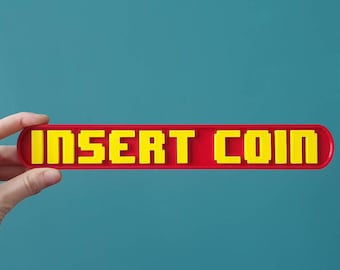 May include: A red plastic sign with the words "INSERT COIN" in yellow block letters.