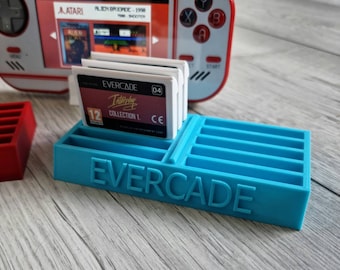May include: A blue plastic game cartridge holder with the word "EVERCADE" printed on the front. The holder has slots for 12 cartridges. There are three game cartridges in the holder, one of which is labeled "EVERCADE 04 Interstellar Collection 1."
