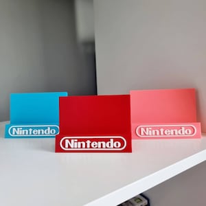 May include: Three Nintendo game cartridge holders, one blue, one red and one pink, with the Nintendo logo in white on each.