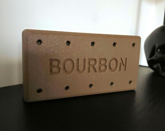 May include: A rectangular, brown sign with the word "BOURBON" engraved in the center. The sign has a series of evenly spaced holes along the top and bottom edges. The sign is made of a textured material.
