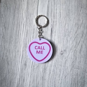 May include: A white heart-shaped keychain with pink trim and the text "CALL ME" in pink letters.