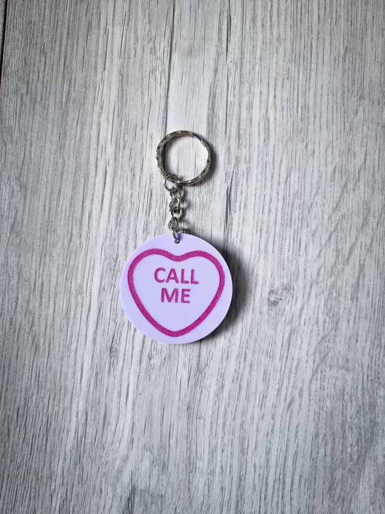 May include: A white heart-shaped keychain with pink trim and the text "CALL ME" in pink letters.