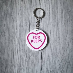 May include: White heart-shaped keychain with a pink outline and the text "FOR KEEPS" in pink letters.
