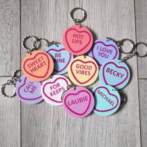 May include: A set of ten heart-shaped keychains with various sayings and names. The keychains are made of a soft, colorful material and feature a pink, red, orange, yellow, blue, and purple color scheme. The keychains are perfect for adding a touch of personality to your keys or bag.