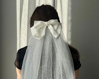 May include: A white tulle veil with a satin bow. The veil has a delicate sparkle throughout.