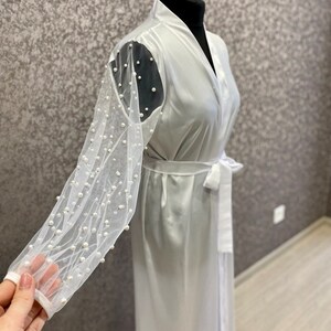 May include: White satin robe with long sleeves featuring a sheer mesh overlay adorned with pearl embellishments.