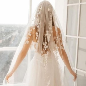 May include: A white bridal veil with delicate floral lace appliques. The veil is made of soft tulle and has a single-tier design.