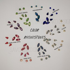 May include: Assortment of marquise-shaped rhinestones in various colors, including aquamarine, light green, purple, dark pink opal, sapphire, clear, white opal, pink opal, and light blue opal. The rhinestones are arranged in groups by color on a white surface. The text "COLOR RHINESTONES" is written in black letters on the white surface.