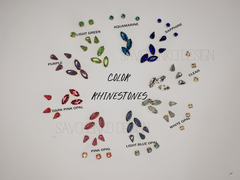May include: Assortment of marquise-shaped rhinestones in various colors, including aquamarine, light green, purple, dark pink opal, sapphire, clear, white opal, pink opal, and light blue opal. The rhinestones are arranged in groups by color on a white surface. The text "COLOR RHINESTONES" is written in black letters on the white surface.