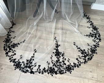 May include: A white tulle wedding veil with a black floral lace trim. The lace is a delicate vine design with small black flowers.