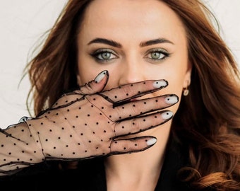 May include: A woman with long brown hair wearing a black polka dot mesh glove over her mouth.