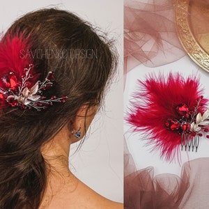 May include: A red feather hair comb with silver and red crystal embellishments. The comb is on a white surface with a red and gold fabric in the background.
