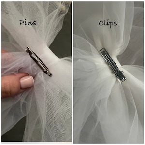 May include: Two images showing two different ways to attach a tulle bow to a fabric item. The first image shows a safety pin attached to the tulle bow. The second image shows a clip attached to the tulle bow. The text "Pins" is above the first image and the text "Clips" is above the second image.