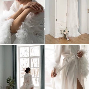 May include: A white satin robe with feather trim on the sleeves and cuffs. The robe is tied at the waist with a white sash. The robe is worn by a person standing in front of a window.
