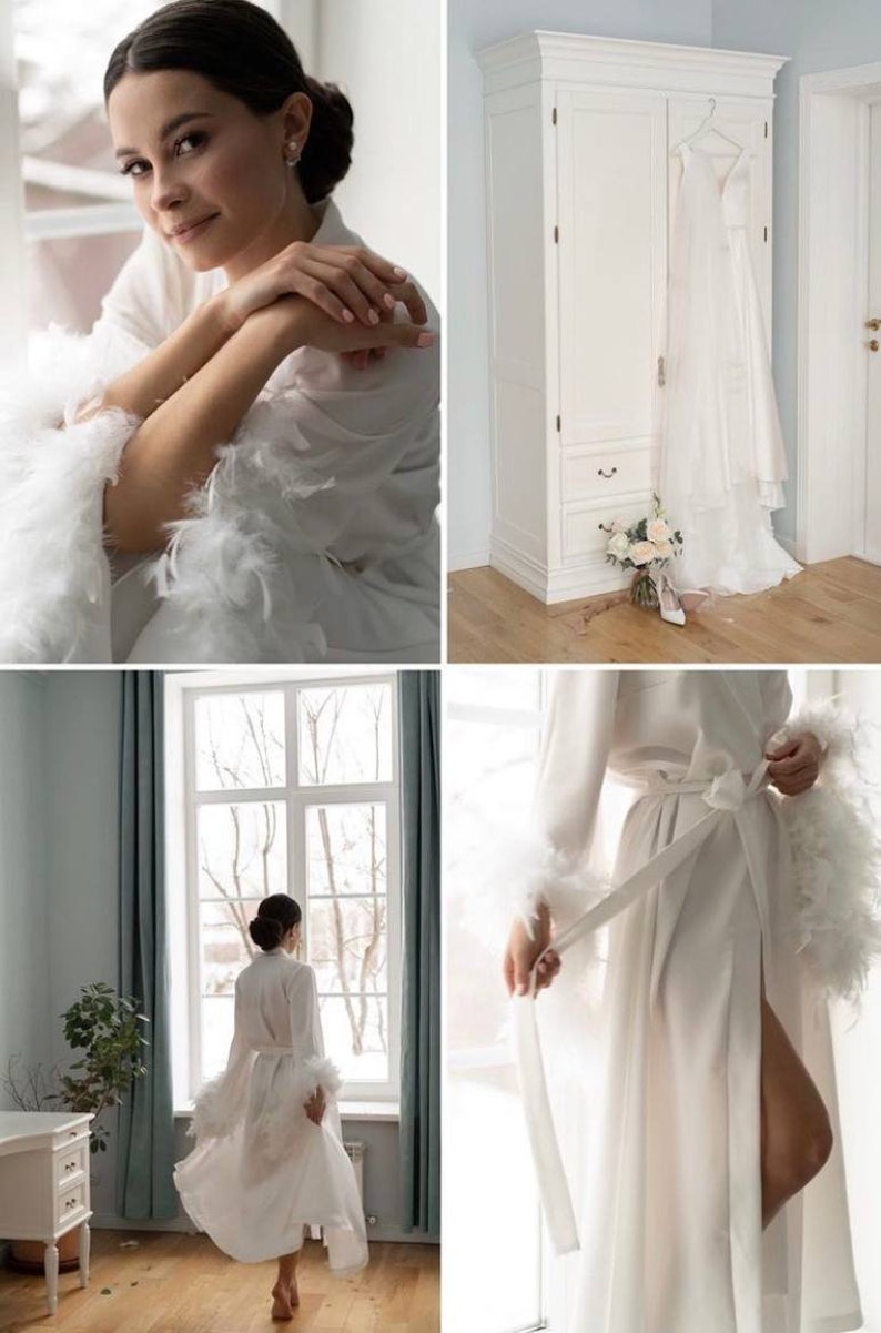 May include: A white satin robe with feather trim on the sleeves and cuffs. The robe is tied at the waist with a white sash. The robe is worn by a person standing in front of a window.