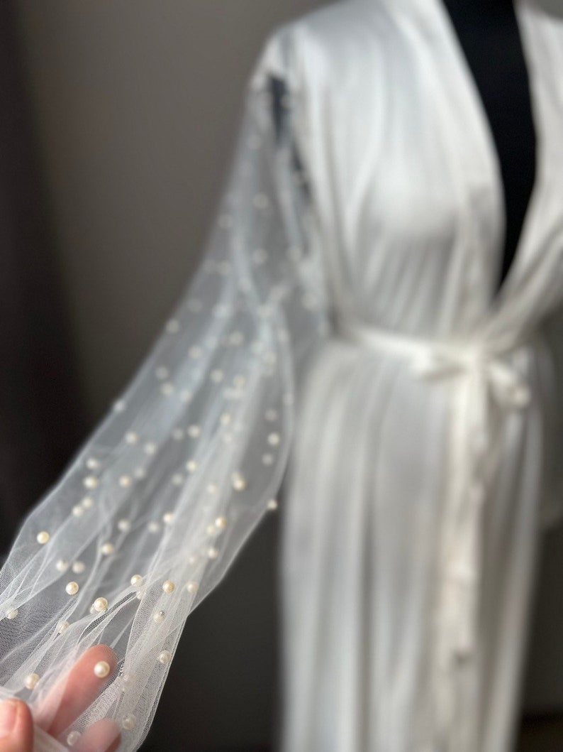 May include: A white sheer robe with pearl embellishments on the sleeves. The robe has a sash tie at the waist.