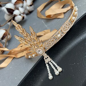 May include: A gold headband with a delicate, leaf-shaped design and a row of pearls. The headband has a dangling pearl drop with three strands of pearls.