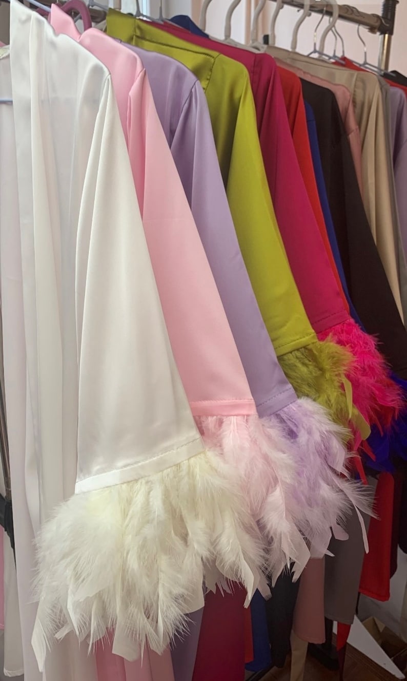 May include: A row of satin robes with feather trim on the sleeves. The robes are in various colours, including white, pink, lavender, green, red, blue, black, and beige.
