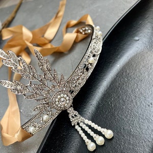 May include: A silver headband with a delicate floral design and pearl accents. The headband is adorned with rhinestones and has a dangling pearl chain.